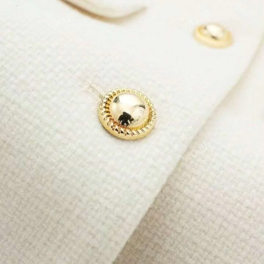 Nahaufnahme der goldenen Knöpfe am weißen Cropped Blazer, freigestellt auf weißem Hintergrund.