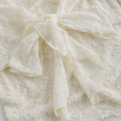 Nahaufnahme der feinen floralen Spitze und der vorderen Schnürung einer cremefarbenen Damenbluse im Boho-Stil mit transparenter Struktur und weichem Faltenwurf
