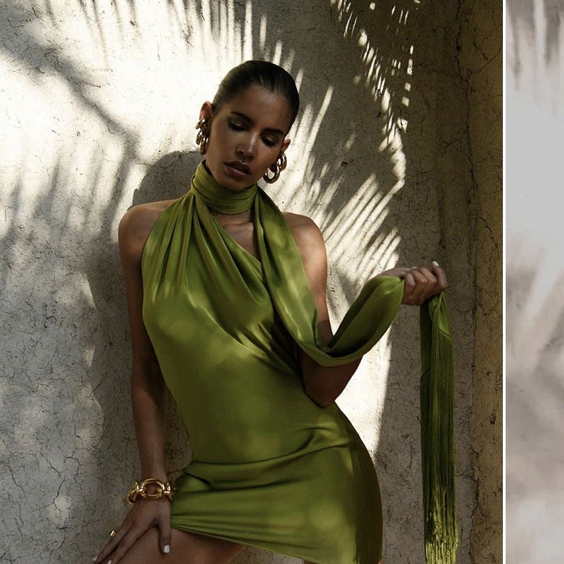 Model trägt das grüne Satin-Minikleid mit Halterneck und hält den passenden Schal mit Fransen locker in der Hand, von vorne fotografiert.