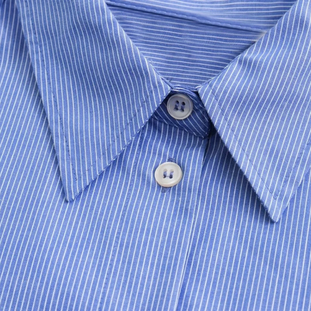 Nahaufnahme des Kragens und der Knopfleiste des blau-weiß gestreiften Damenhemds mit weißen Knöpfen und klassischem Schnitt